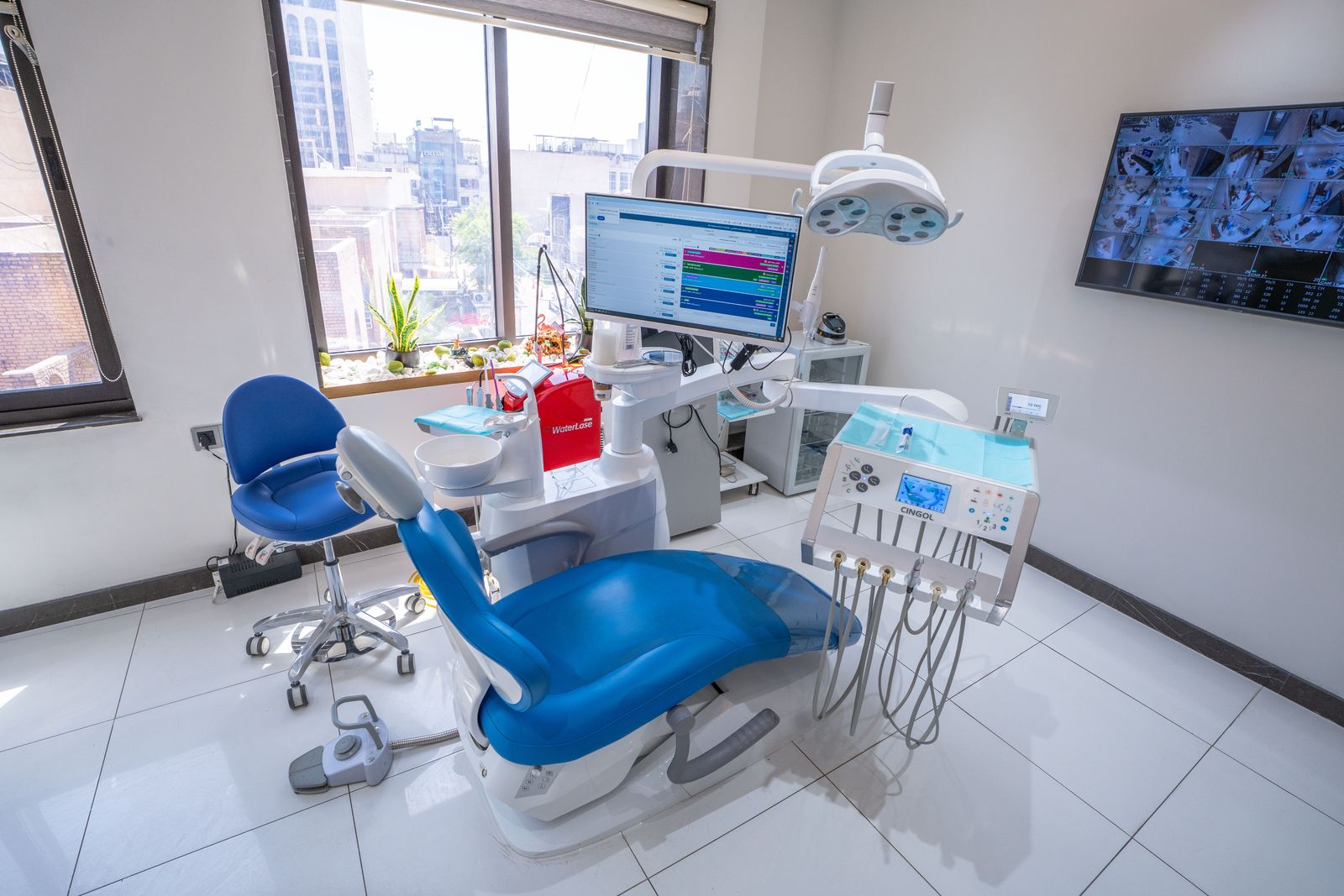 A blue dental chair beside a wall screen showing X-ray images