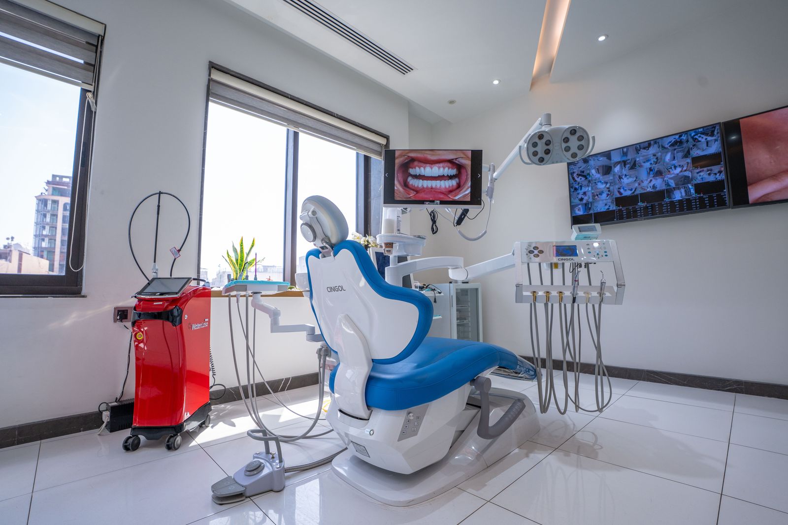 A treatment room with a red dental laser unit beside the chair and wall screens