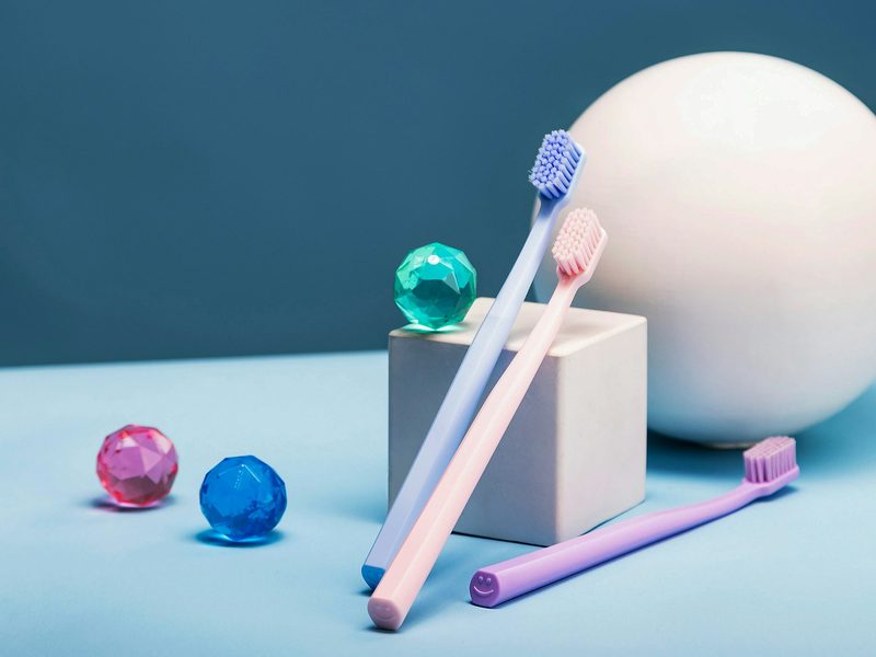 Three pastel toothbrushes beside colourful decorative balls